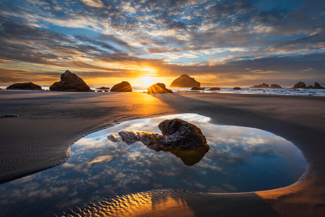 Bandon Beach tide pool sunset reflections with cloudy sky.