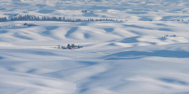 Panoramic image of snow-covered Palouse hills with red barn in the middle.