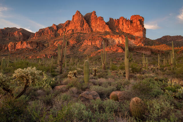 Fine art landscape photograph of the Superstition Mountains near Phoenix, Arizona, at sunset, featuring rugged red rock peaks and a green desert landscape after