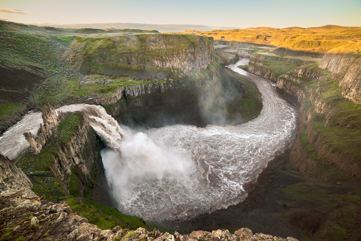 Huge flows of water flow over Palouse Falls in eastern Washington with a view of the Palouse River.